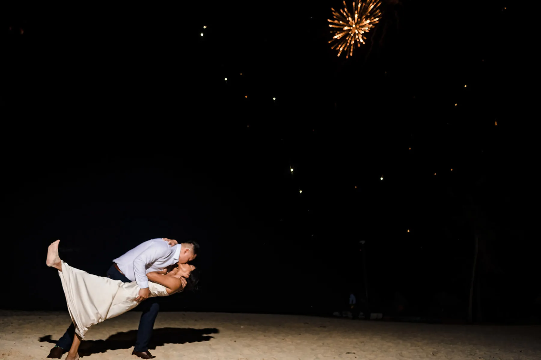 Romantic couple kiss under fireworks display at nighttime beach wedding celebration in Cancun Riviera Maya Mexico