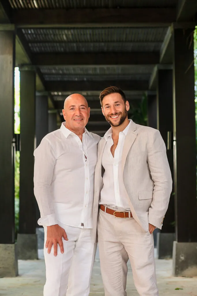 Two grooms in white linen suits posing for wedding photos in modern Cancun resort architecture Riviera Maya Mexico