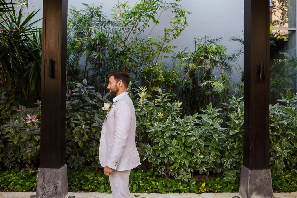 Groom in white linen suit with boutonniere at tropical Riviera Maya wedding venue with lush greenery backdrop