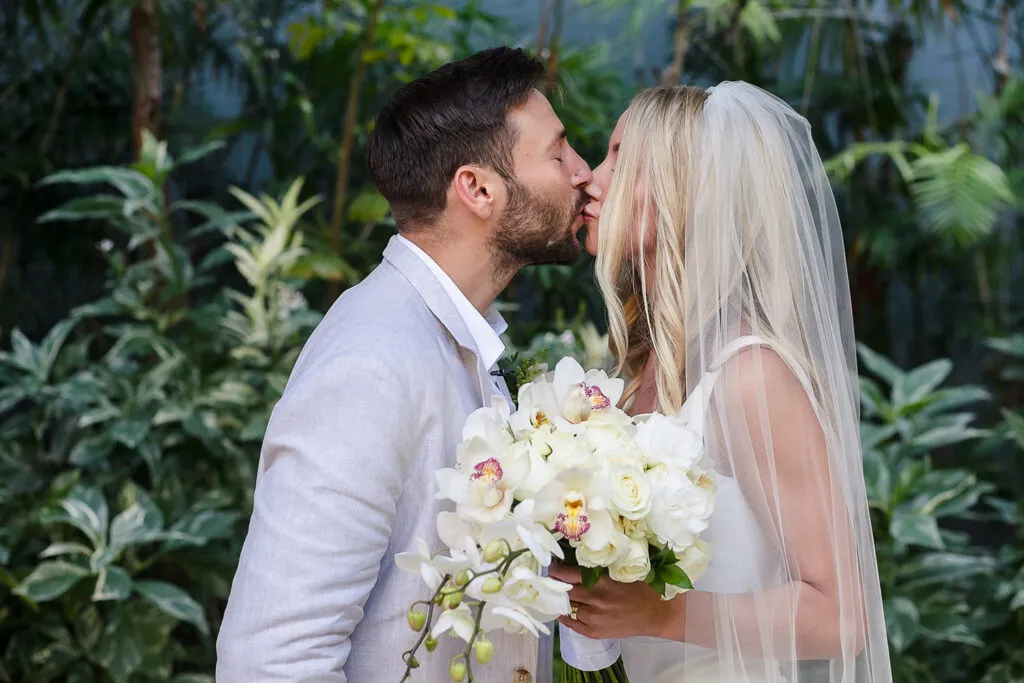 Bride and groom kissing with white orchid bouquet at tropical Cancun wedding ceremony in lush jungle setting