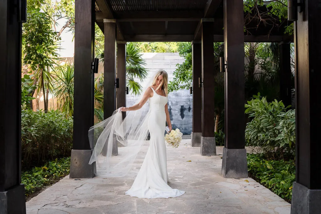 Bride in flowing white wedding dress and veil at luxury Riviera Maya resort surrounded by tropical palm trees in Mexico