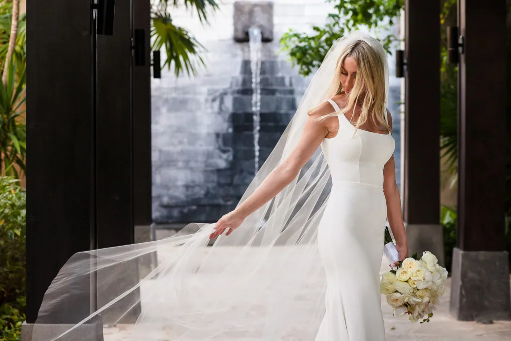 Elegant bride in white gown with flowing veil holding bouquet at luxury Riviera Maya wedding venue in Cancun Mexico