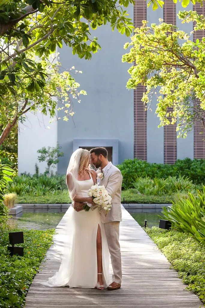 Bride and groom embrace on wooden dock at luxury Riviera Maya resort wedding venue surrounded by tropical landscaping