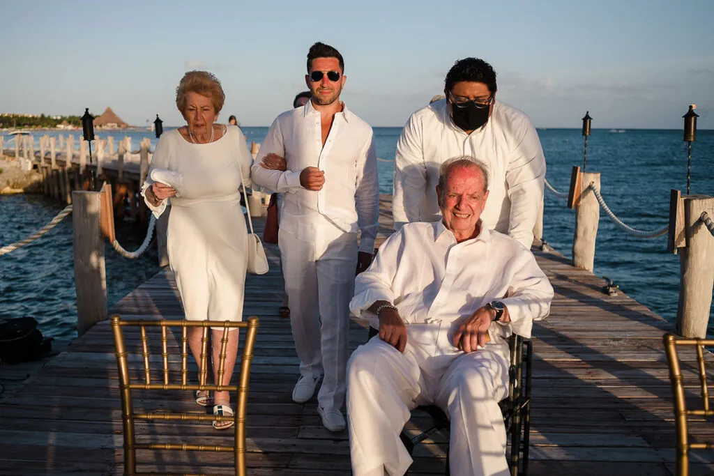 Elegant beach wedding ceremony on wooden dock in Cancun with family members in white attire overlooking Caribbean waters