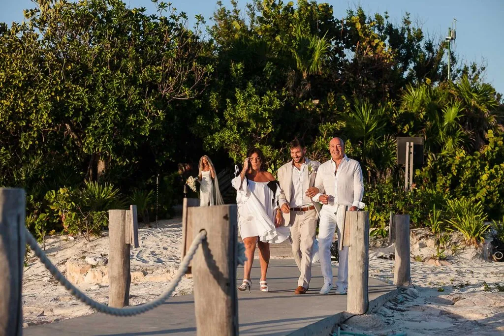 Beach wedding ceremony in Riviera Maya with bride and groom walking down wooden boardwalk surrounded by tropical vegetation