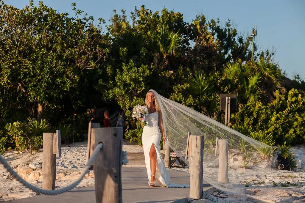 Bride in flowing white dress and veil walking on wooden boardwalk at Riviera Maya beach wedding in Cancun Mexico