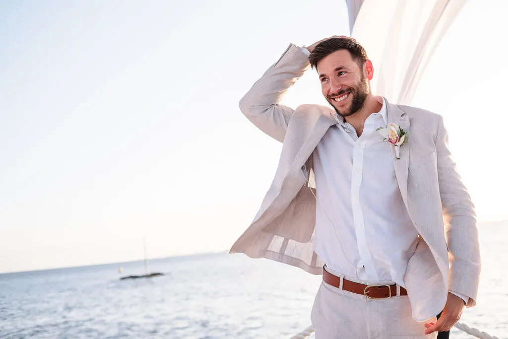 Groom in light linen suit with boutonniere smiling at beach wedding ceremony in Cancun Riviera Maya Mexico