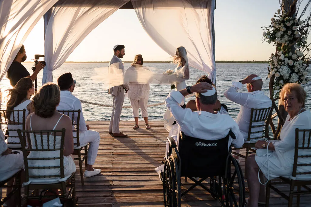 Waterfront wedding ceremony at sunset in Riviera Maya Mexico with couple exchanging vows under white fabric canopy on dock