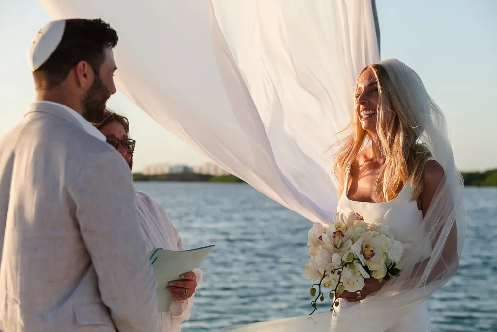 Beach wedding ceremony in Cancun with bride and groom exchanging vows under white draping by turquoise Caribbean waters