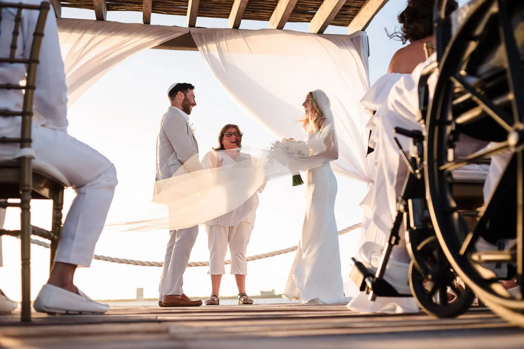 Nautical wedding ceremony on yacht deck in Cancun with bride, groom and officiant under flowing white canopy at sunset