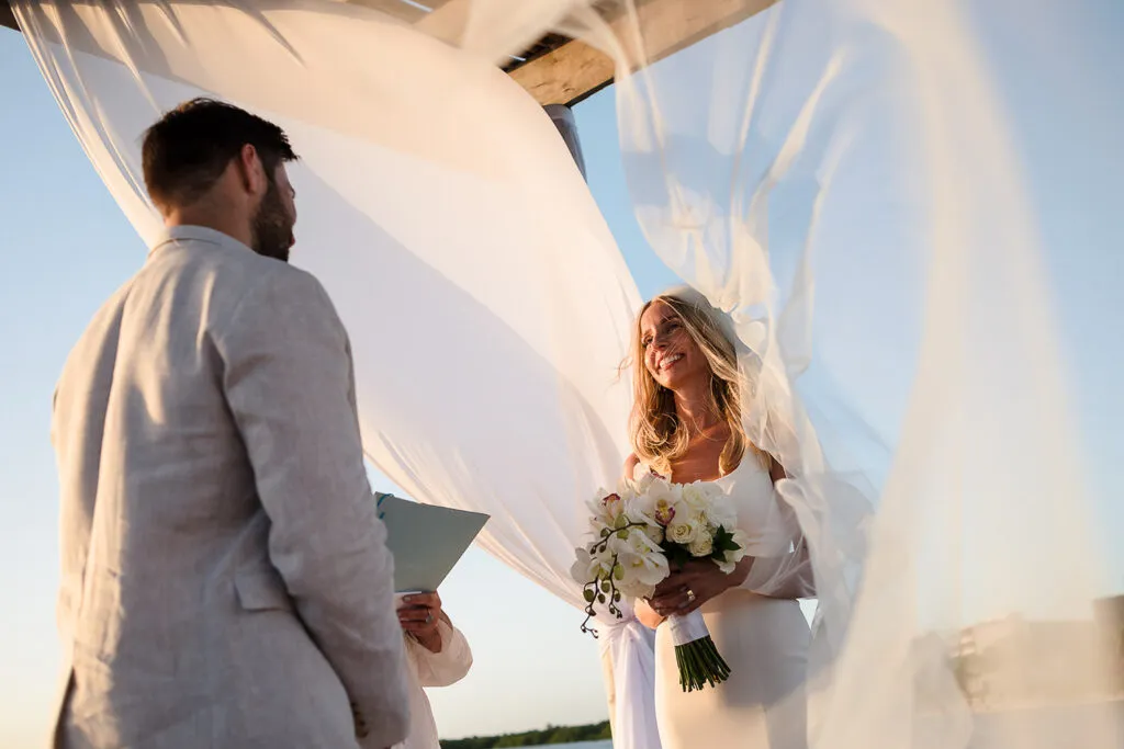 Bride and groom exchanging vows under flowing white fabric canopy during romantic beach wedding ceremony in Cancun Mexico