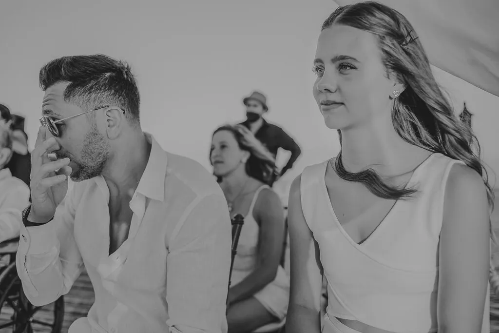 Emotional groom wiping tears during beach wedding ceremony in Cancun Mexico with bride and guests celebrating love