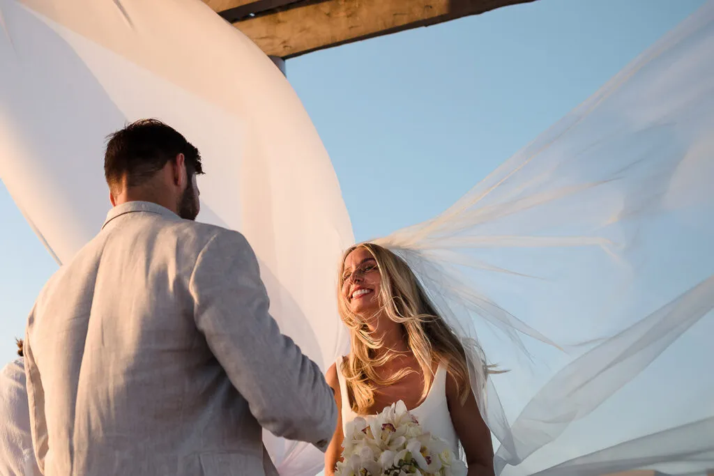 Bride and groom exchanging vows under flowing white fabric canopy during sunset wedding ceremony in Cancun Mexico