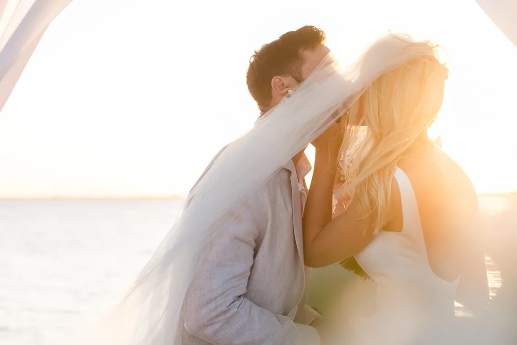 Romantic bride and groom kissing under veil at sunset beach wedding in Cancun Riviera Maya Mexico destination photography