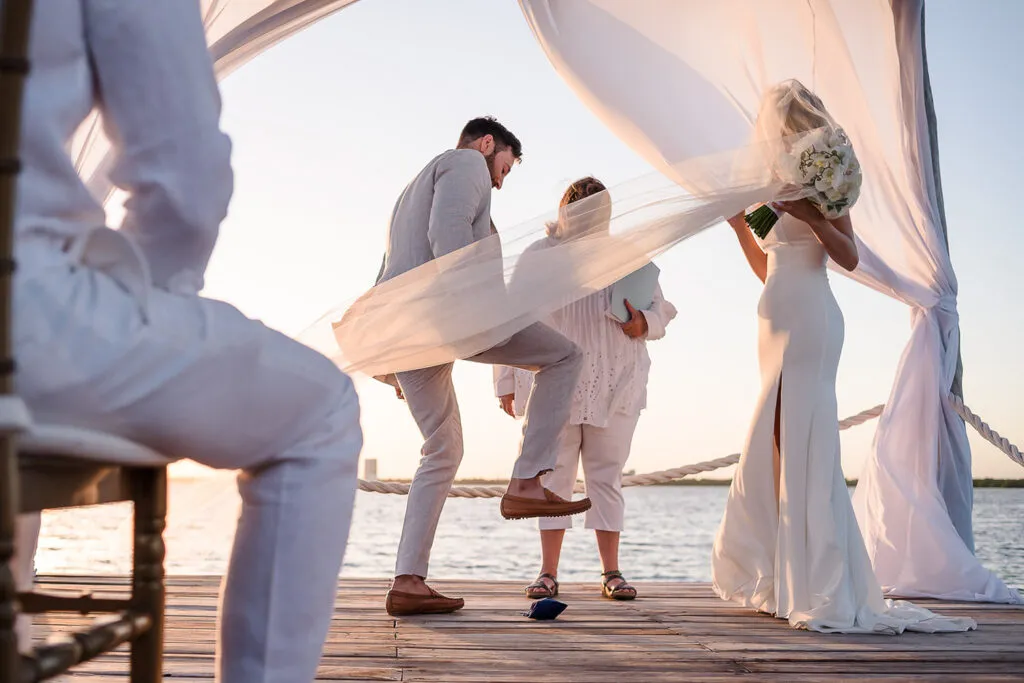 Beach wedding ceremony in Cancun with bride, groom and child under flowing white fabric canopy at sunset on wooden dock