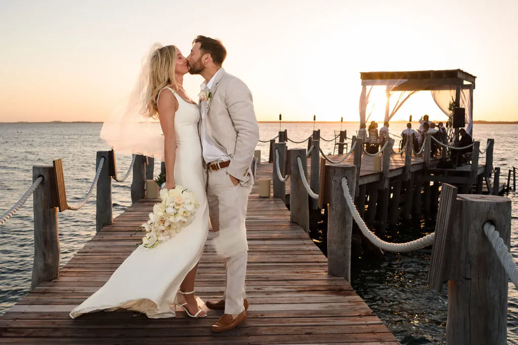 Romantic sunset wedding kiss on wooden dock in Riviera Maya Mexico with ocean views and tropical ceremony backdrop
