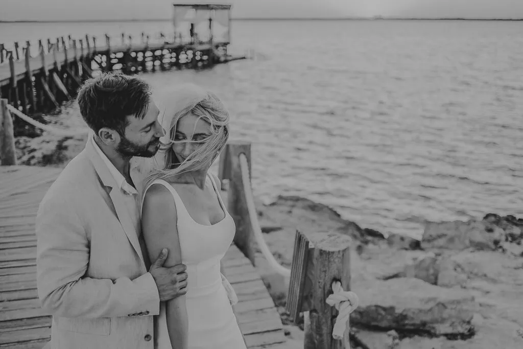 Romantic couple embracing on wooden pier in Cancun - intimate destination wedding photography session by the Caribbean Sea