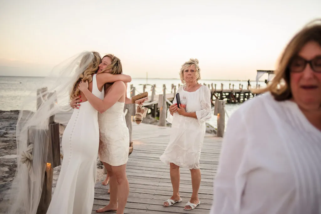 Bride hugging wedding guest on waterfront dock during sunset ceremony in Cancun Riviera Maya Mexico beach wedding photography
