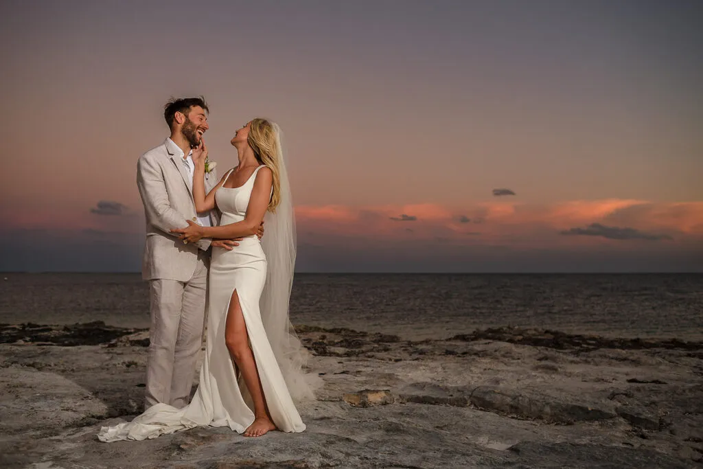Romantic beach wedding couple embracing at sunset in Cancun Mexico with bride in white dress and groom in linen suit