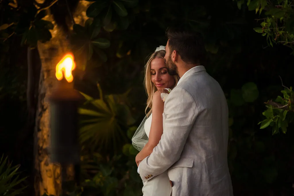 Romantic couple embracing at twilight wedding in Cancun with tropical foliage and warm lighting, Riviera Maya photography