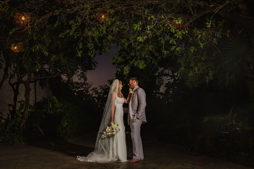Romantic bride and groom portrait under twinkling lights in lush tropical garden at Riviera Maya wedding venue Mexico
