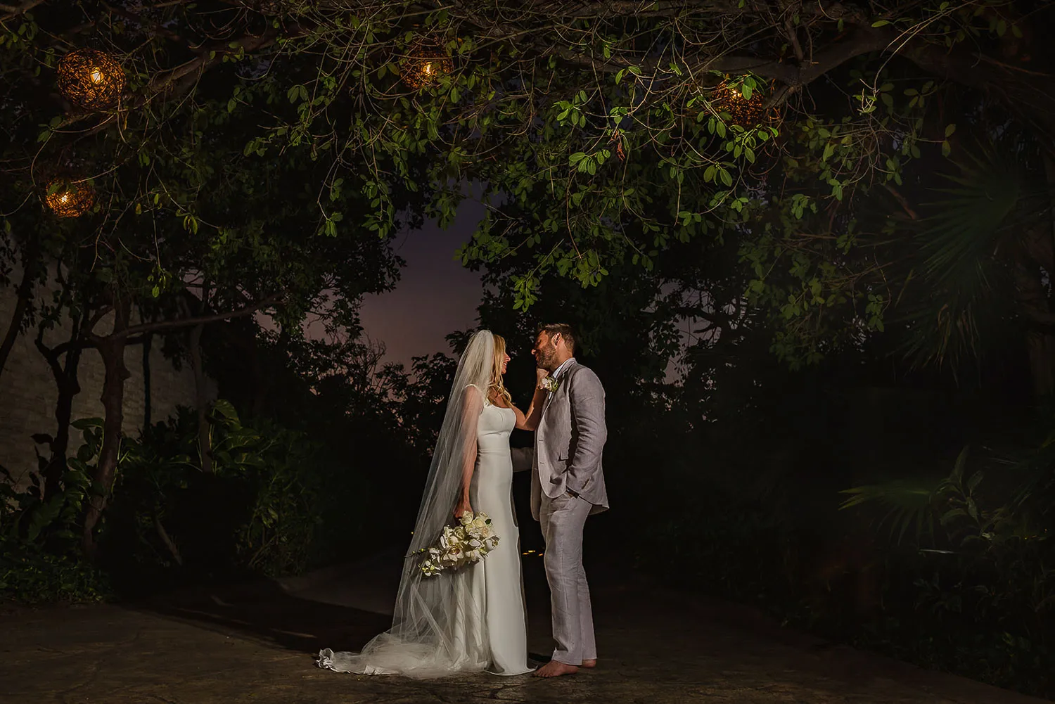 Romantic bride and groom portrait under twinkling lights in lush tropical garden at Riviera Maya wedding venue Mexico