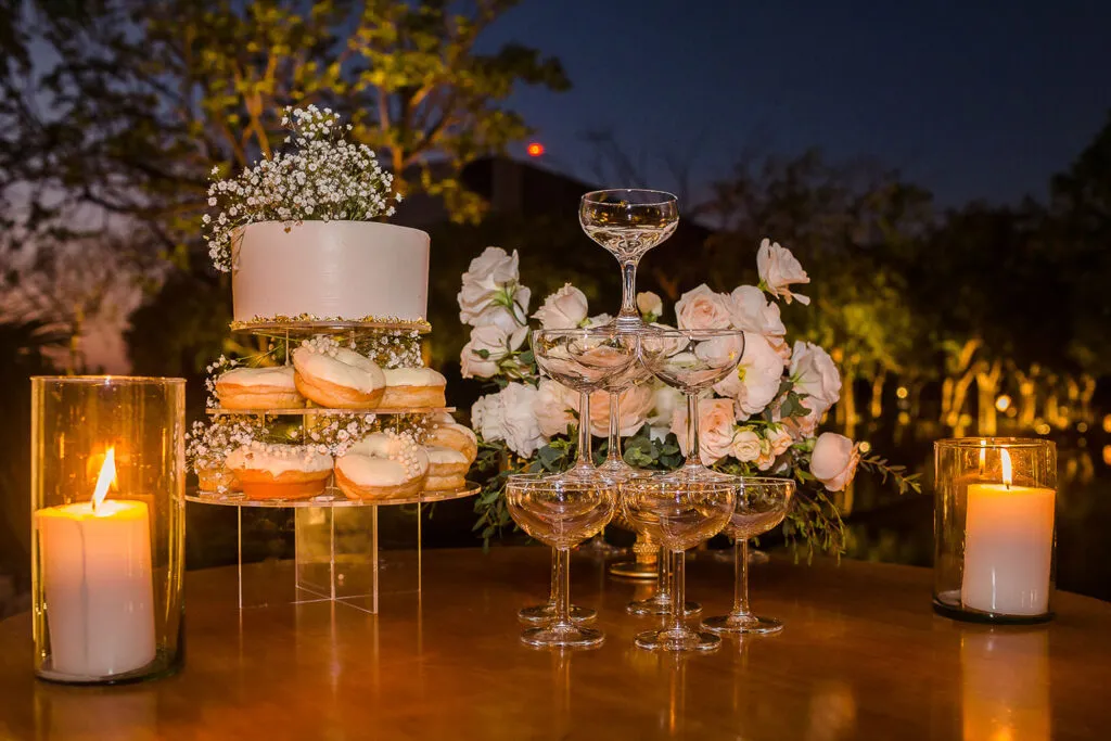 Elegant wedding cake and champagne tower at sunset reception in Riviera Maya Mexico with candles and pink roses