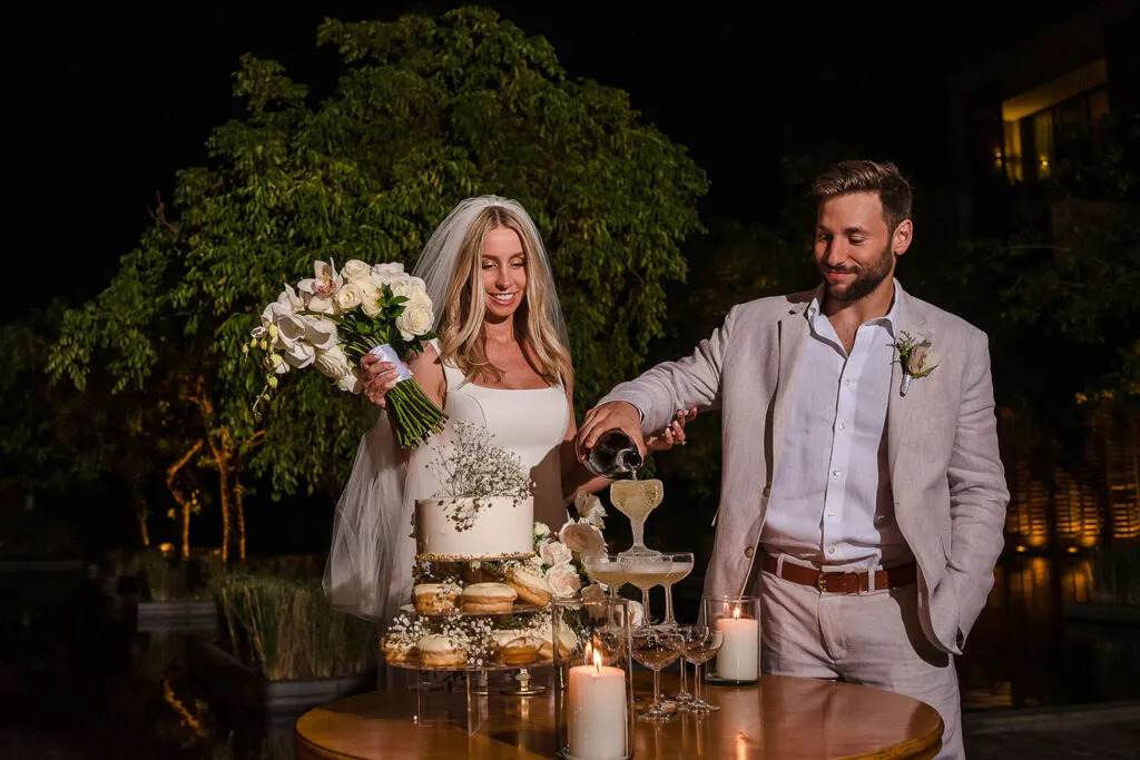 Newlyweds pouring champagne at their romantic Cancun wedding reception with cake and candles under tropical evening sky
