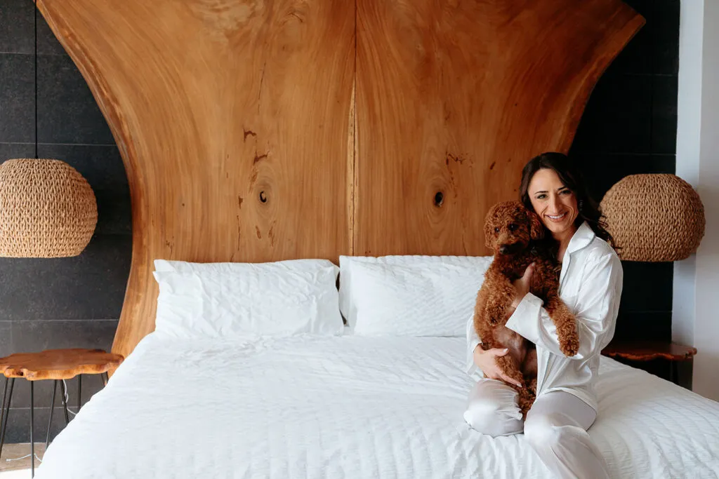 Bride in white robe holding poodle on bed at luxury Riviera Maya resort before Cancun destination wedding photography