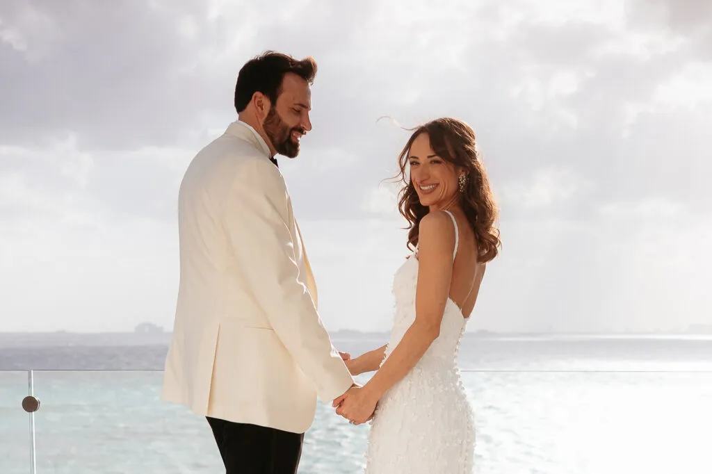 Romantic bride and groom holding hands at sunset wedding ceremony in Cancun with ocean view and cloudy sky backdrop