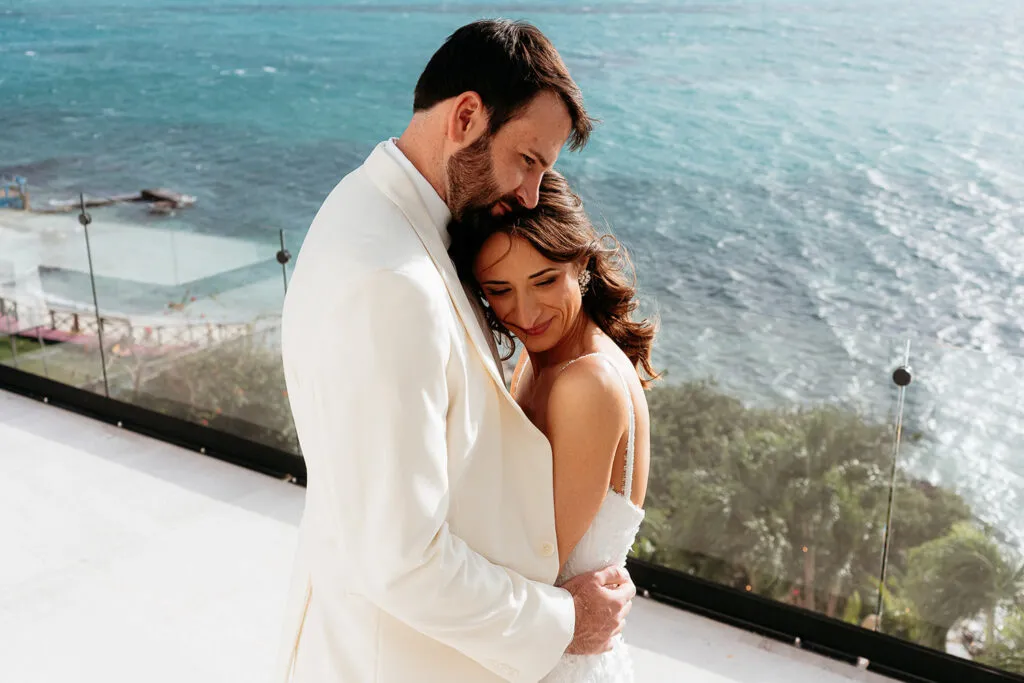 Romantic wedding couple embracing on oceanfront terrace overlooking turquoise Caribbean Sea in Cancun Riviera Maya Mexico