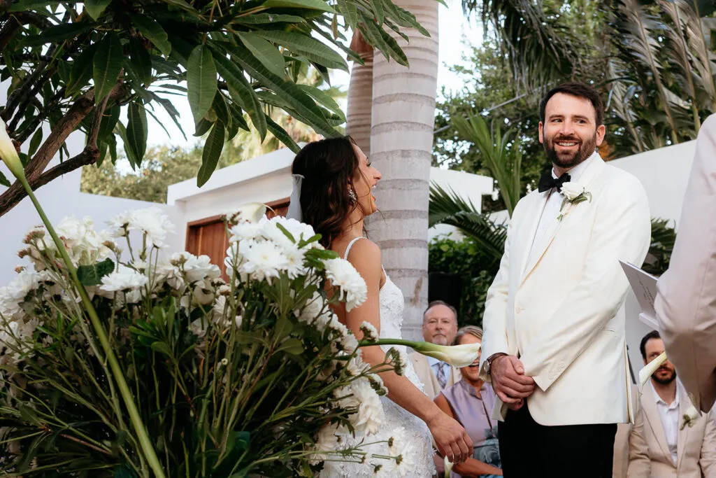 Tropical wedding ceremony in Riviera Maya with bride and groom exchanging vows surrounded by palm trees and white flowers