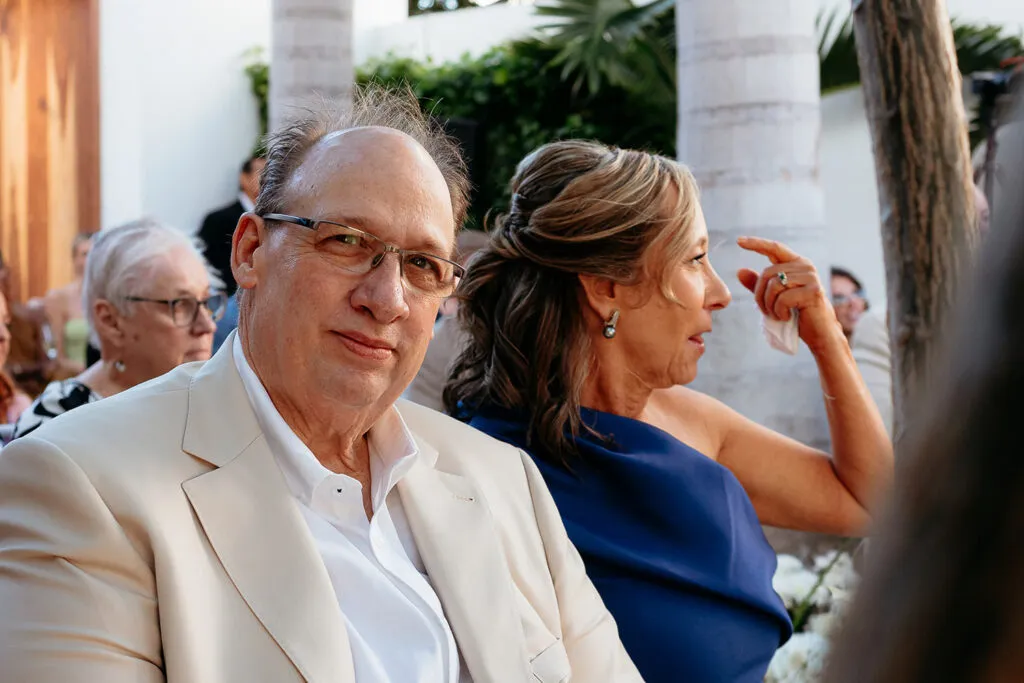 Elegant wedding guests at luxury Riviera Maya ceremony with tropical palm trees and white columns in background