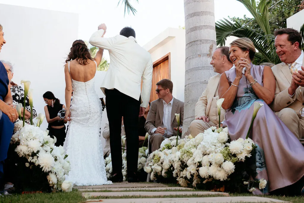 Tropical wedding ceremony in Cancun with bride and groom celebrating surrounded by white flowers and palm trees