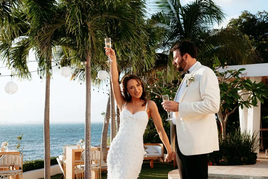 Bride and groom celebrating with champagne toast at tropical Riviera Maya beachfront wedding ceremony in Mexico