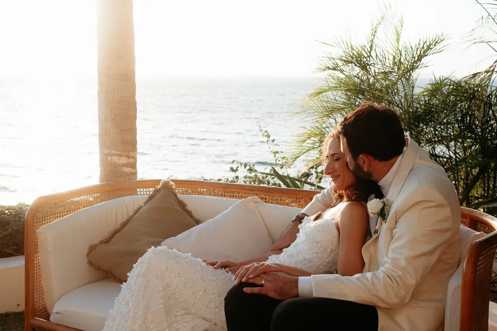 Romantic newlyweds sharing intimate moment on beach sofa during golden hour wedding photography session in Cancun Mexico