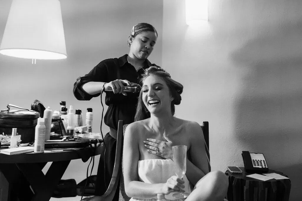 Bride getting ready with hairstylist in Micro wedding in cancun Bridal  suite with champagne and beauty products
