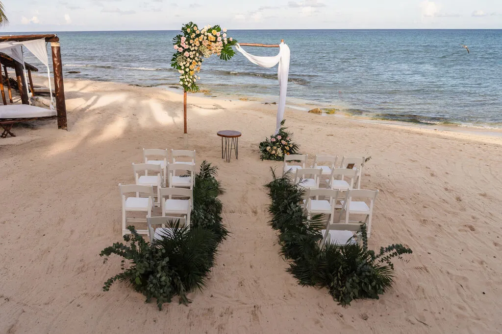 Beach wedding ceremony setup in cancun with floral arch, white chairs, and tropical greenery overlooking Caribbean Sea