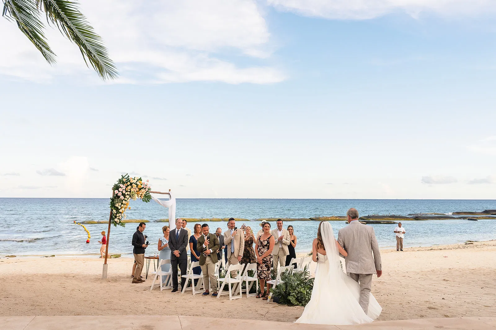Beach Microwedding ceremony in cancun Mexico with bride walking down aisle toward floral arch and ocean backdrop
