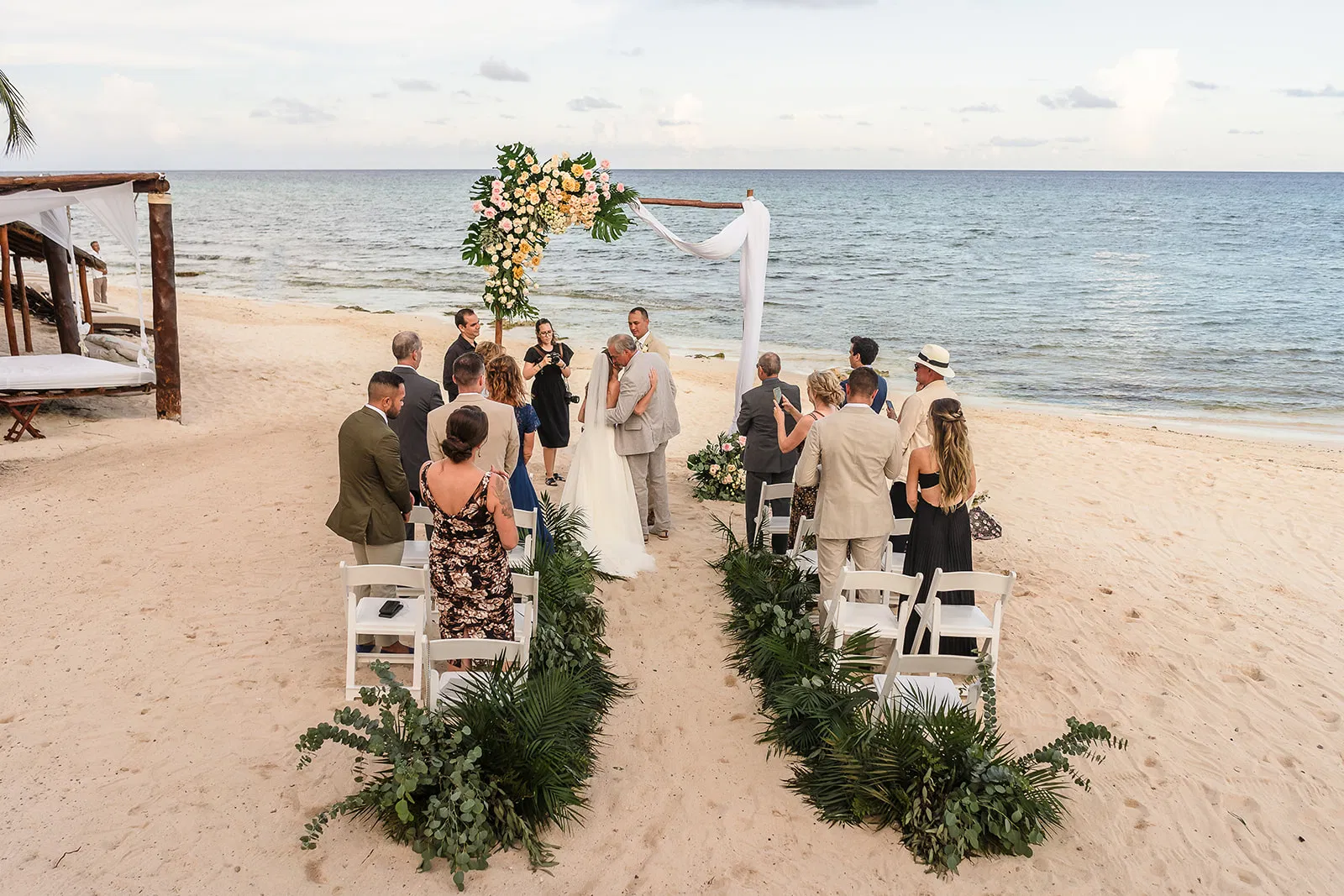 Beach wedding ceremony in Tulum Mexico with tropical floral arch and ocean backdrop - destination wedding photography