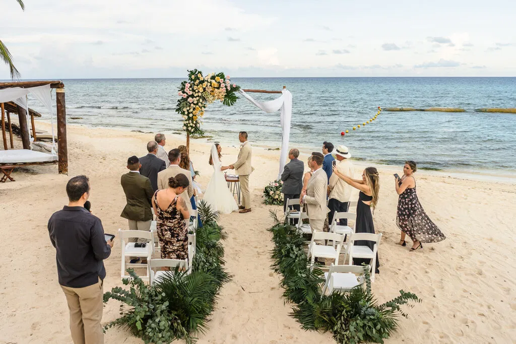 micro wedding ceremony in Cancun Mexico with tropical floral arch and guests on white sand overlooking Caribbean Sea