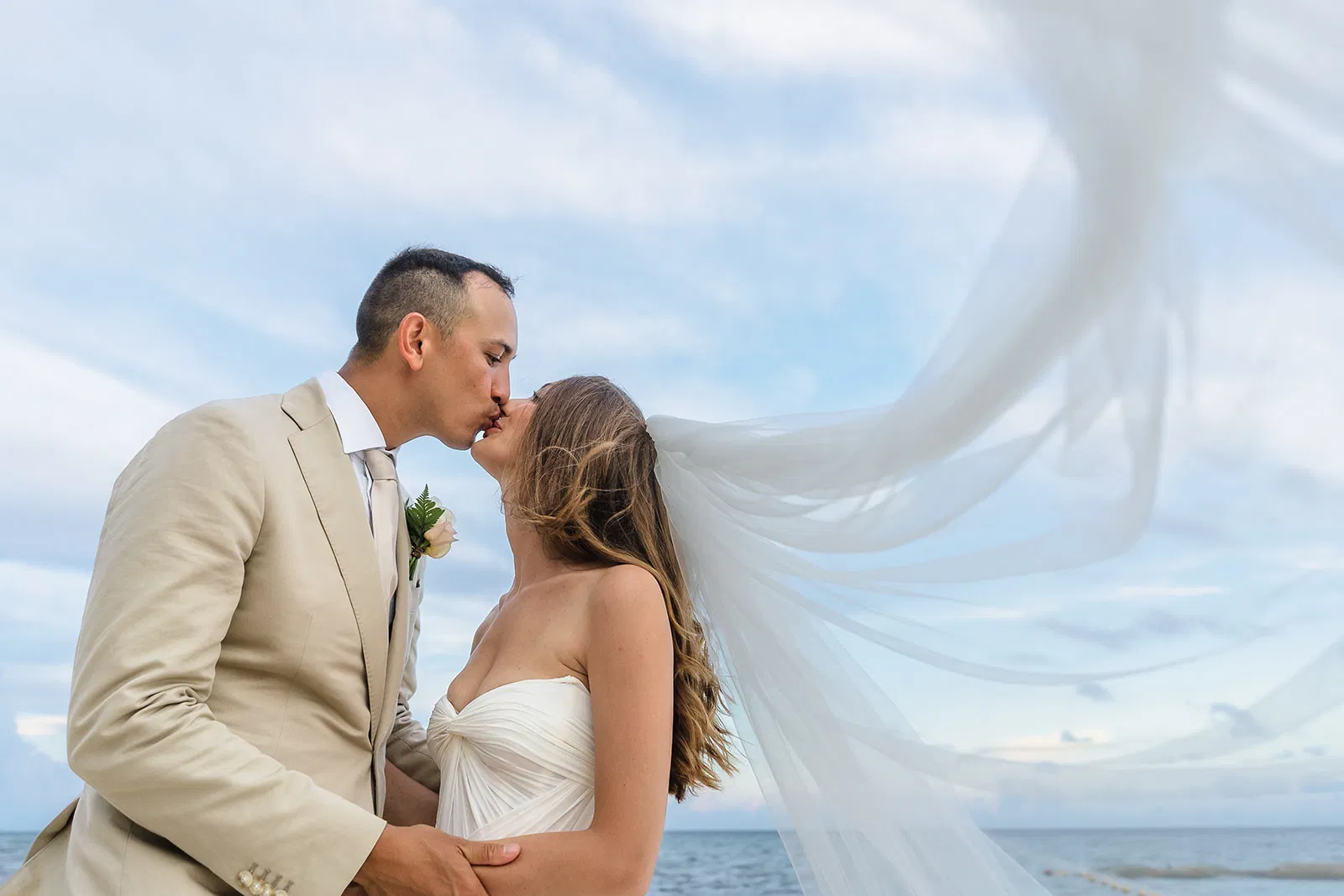 Romantic bride and groom kissing on beach with flowing veil in Tulum Mexico destination wedding photography