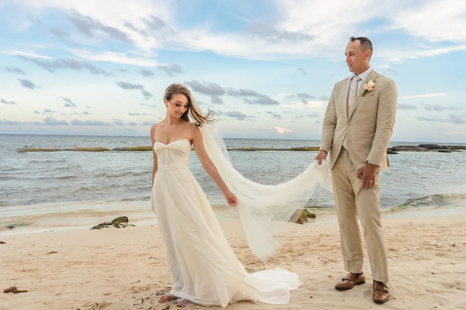 Bride and groom beach wedding portrait in Tulum Mexico with flowing veil and beige suit on tropical coastline