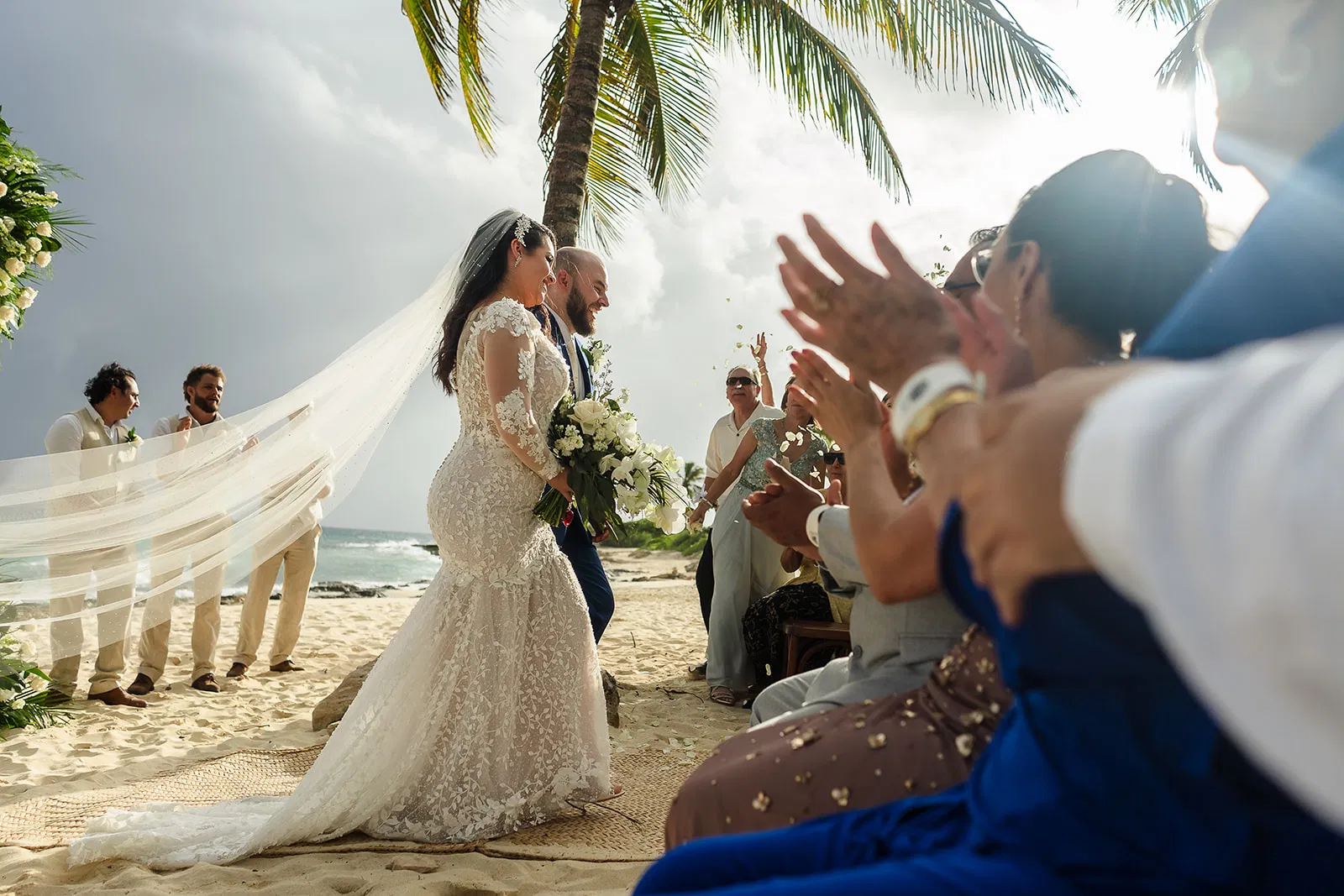 Couple sharing first kiss at beach ceremony while guests applaud at Hotel Xcaret wedding in Riviera Maya