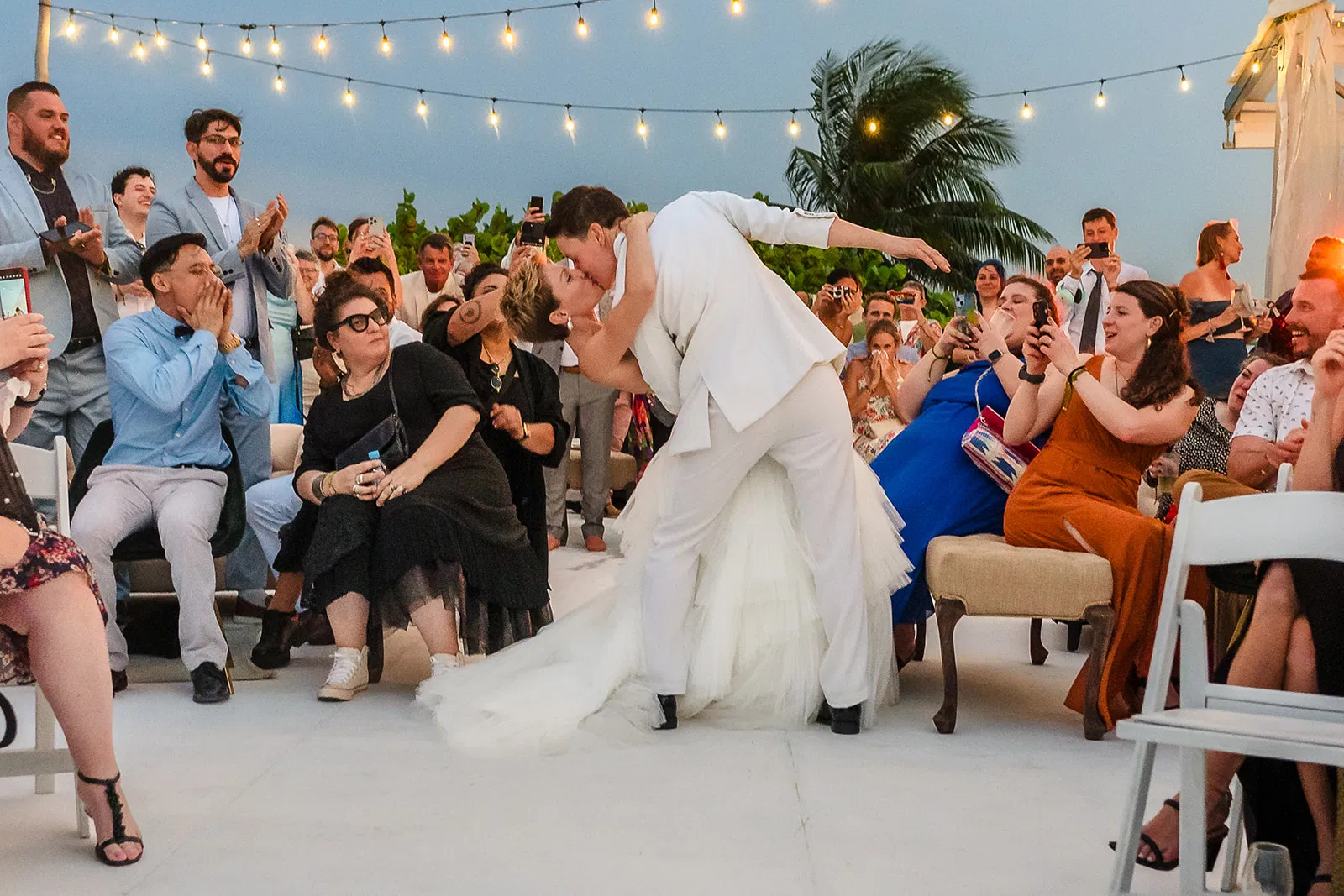 Two brides sharing a kiss during outdoor wedding ceremony in Riviera Maya Mexico with guests cheering
