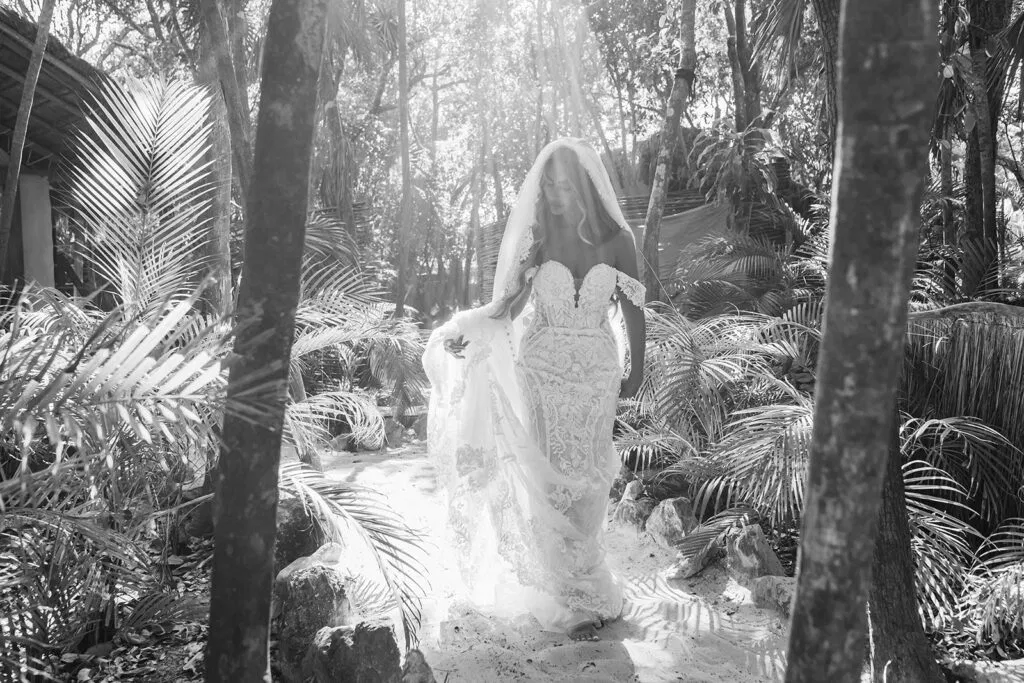 Bride in elegant wedding dress and veil walking through tropical jungle palms in Tulum Mexico for romantic wedding photos