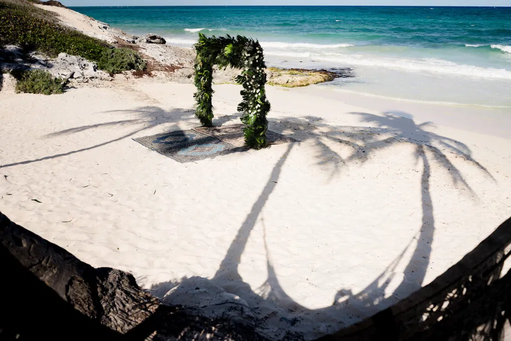 Tropical beach wedding ceremony setup with floral arch and ocean views in Tulum Mexico destination wedding photography