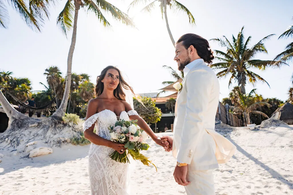 Bride and groom holding hands on Tulum beach with palm trees, destination wedding photography in Mexico's Caribbean coast