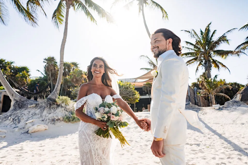 Newlywed couple running hand in hand on Tulum beach after destination wedding ceremony with palm trees and white sand
