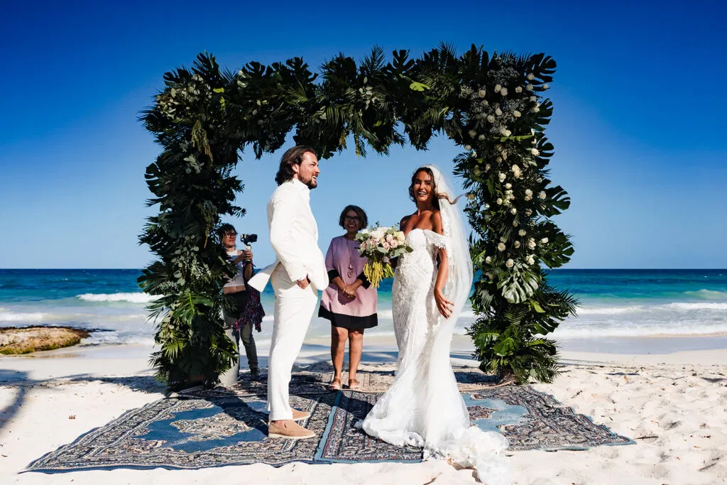 Beach wedding ceremony in Tulum Mexico with tropical arch, bride and groom on white sand with turquoise ocean backdrop